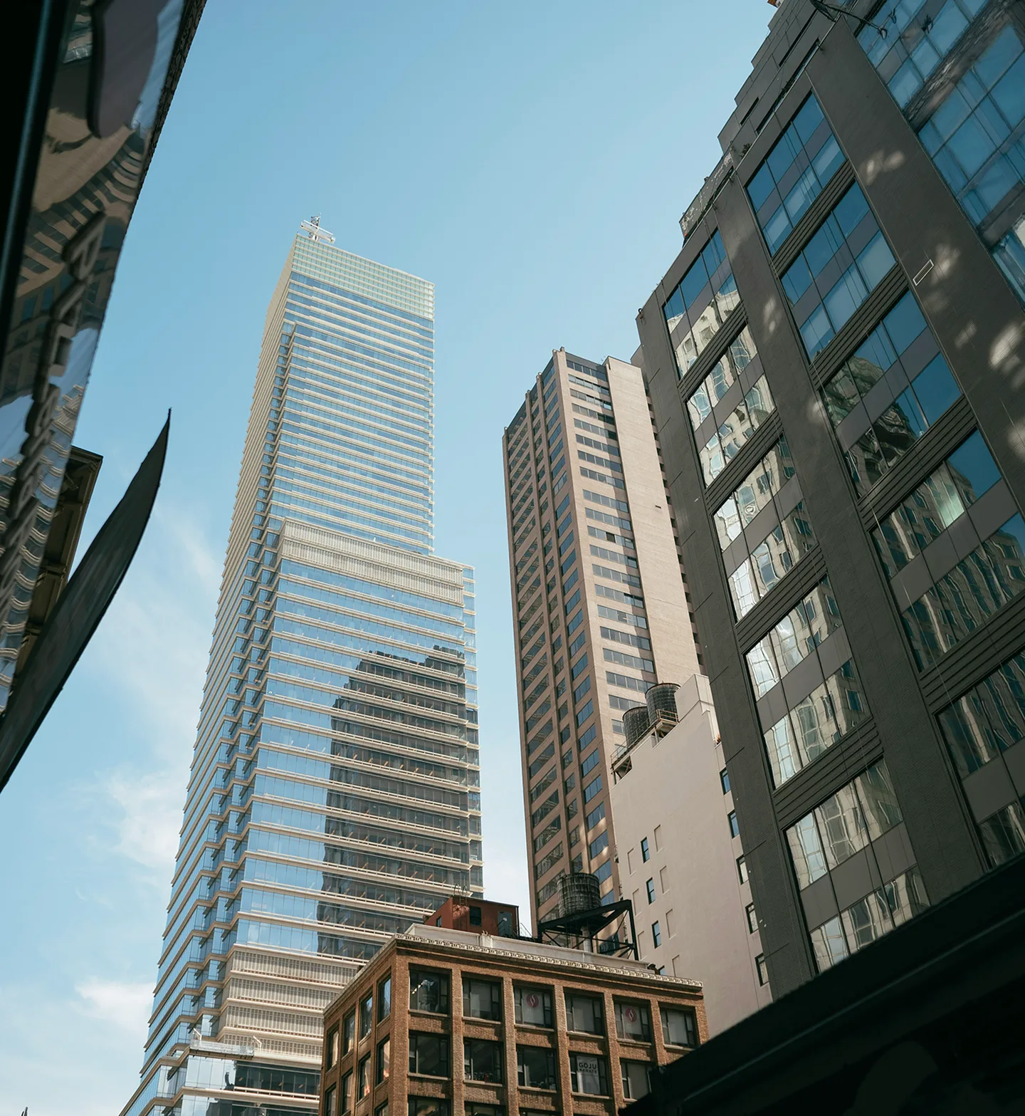 A glass tower rising over lower buildings, seen from street level